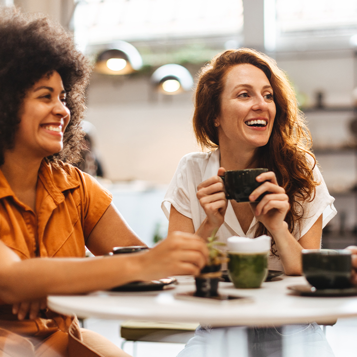 Two people sitting at a table smiling holding a coffee mug