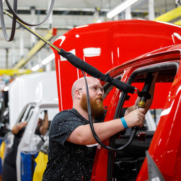 Manufacturing worker using machinery on red automobile within factory line