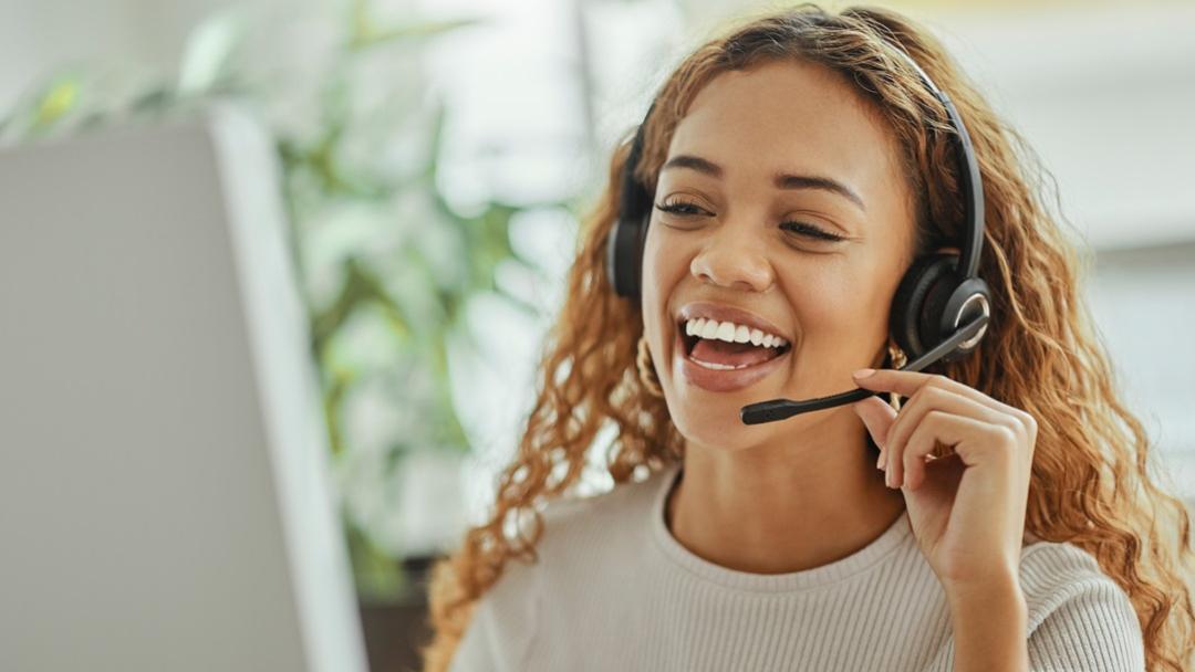 Woman in business attire talking into a headset in front of a computer screen