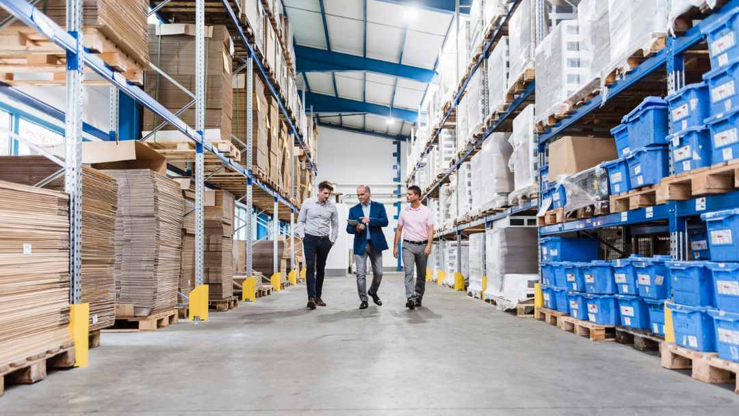 Three warehouse workers walking down a warehouse aisle 