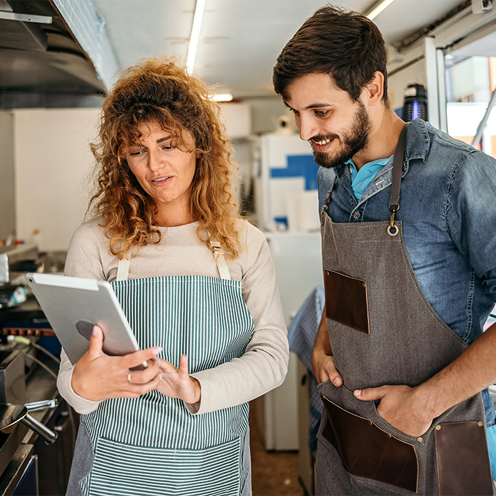 two people wearing aprons looking at an tablet