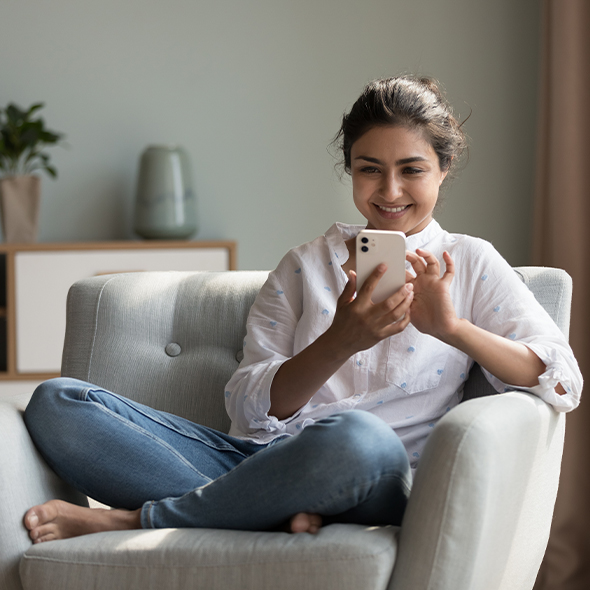 woman sitting cross-legged in armchair using a mobile phone