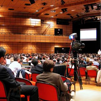 auditorium of people looking at a stage with a camera recording