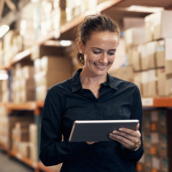 woman in warehouse smiling at tablet in her hand