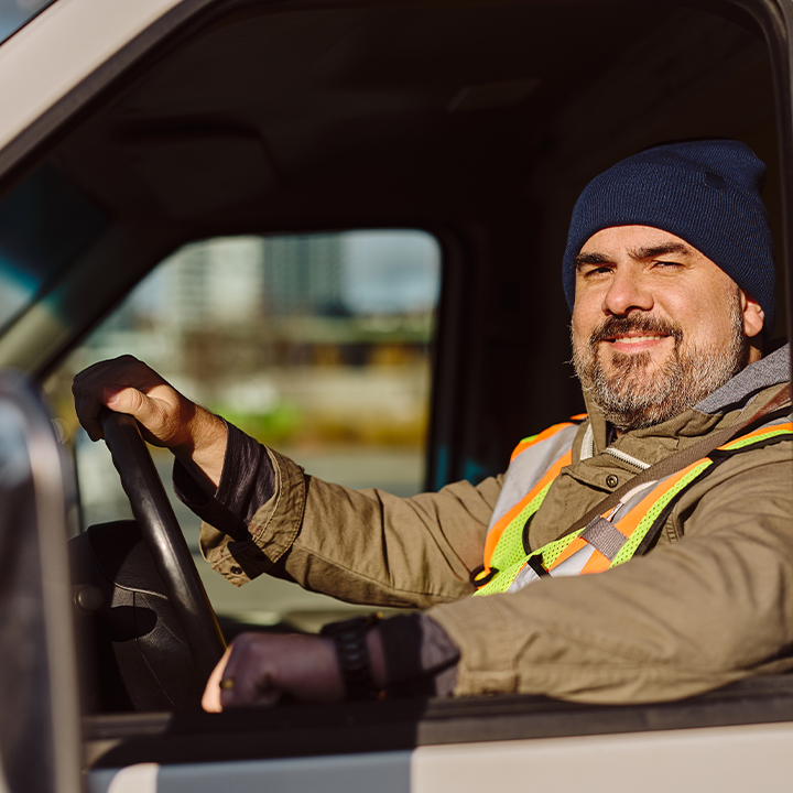 man wearing a beanie and reflective vest driving a truck