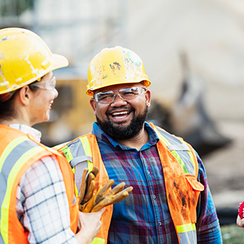 two construction workers wearing yellow hard hats and reflective vests laughing