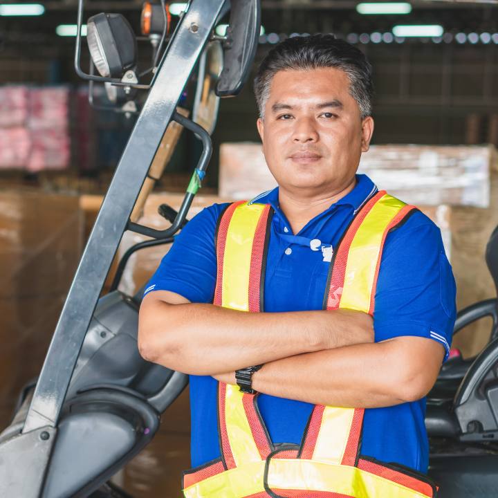 man wearing a reflective vest standing in front of a forklift