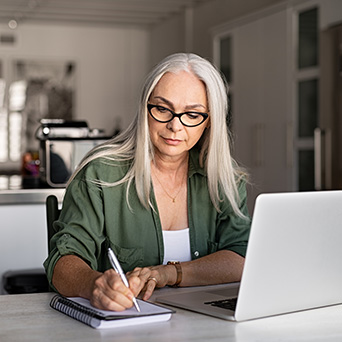 woman writing on a notepad next to a laptop