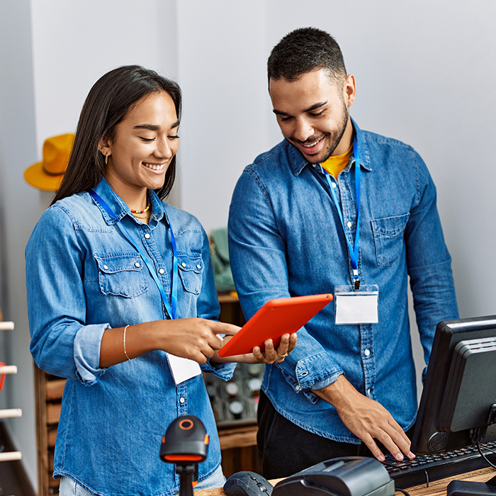 two people working behind a desk looking at a tablet