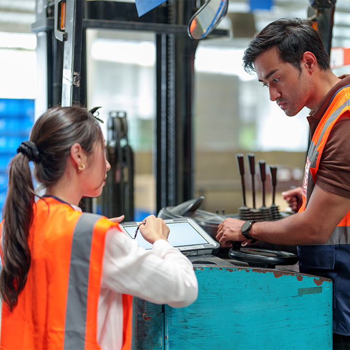 woman in a reflective vest talking to someone on a stand up forklift